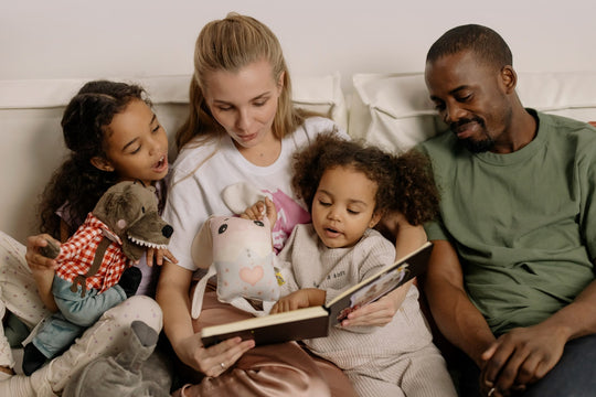 A mixed race family reads a story to two young children on a couch.